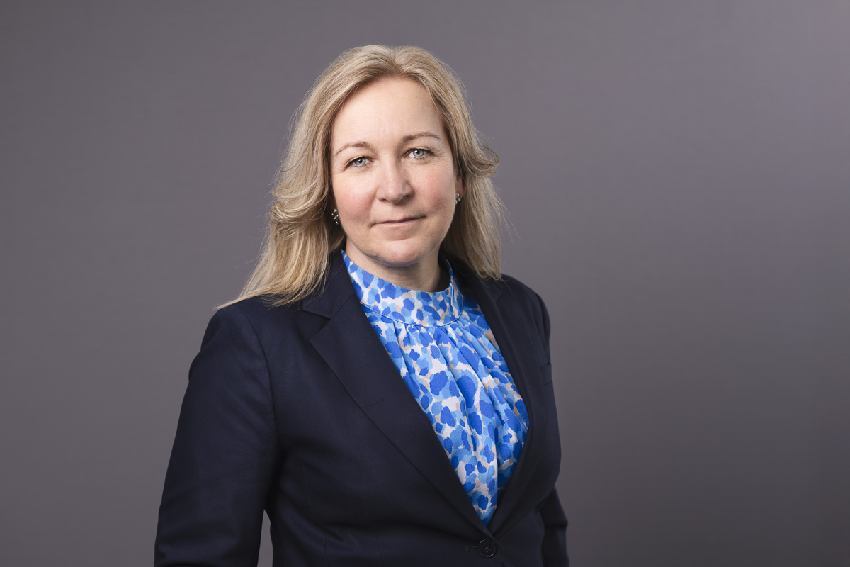 En blond kvinna med svart kavaj och blåmönstrad blus