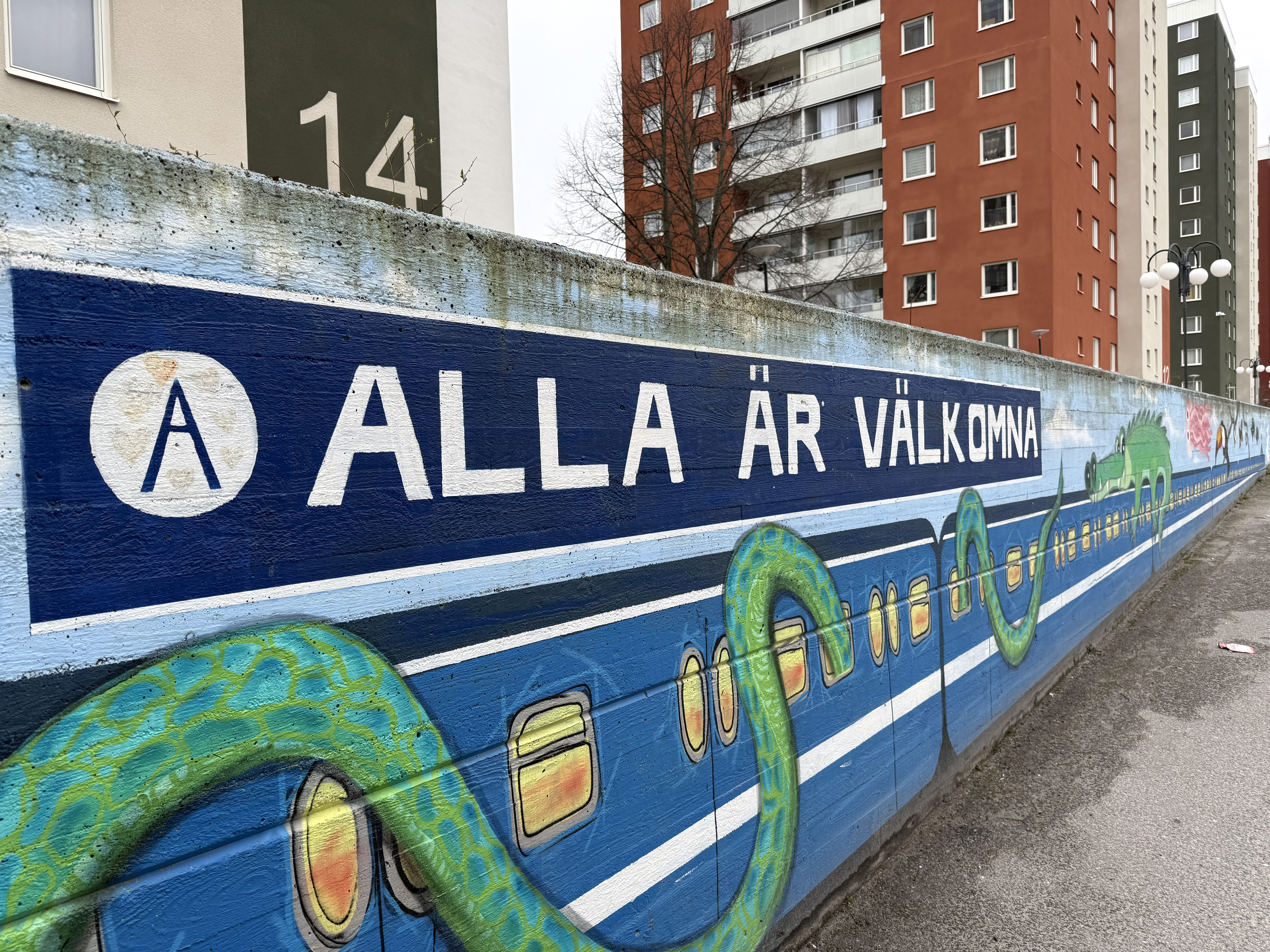 Målning på mur med orm som slingrar sig runt tunnelbanetåg, i bakgrunden syns flera färgglada höghu